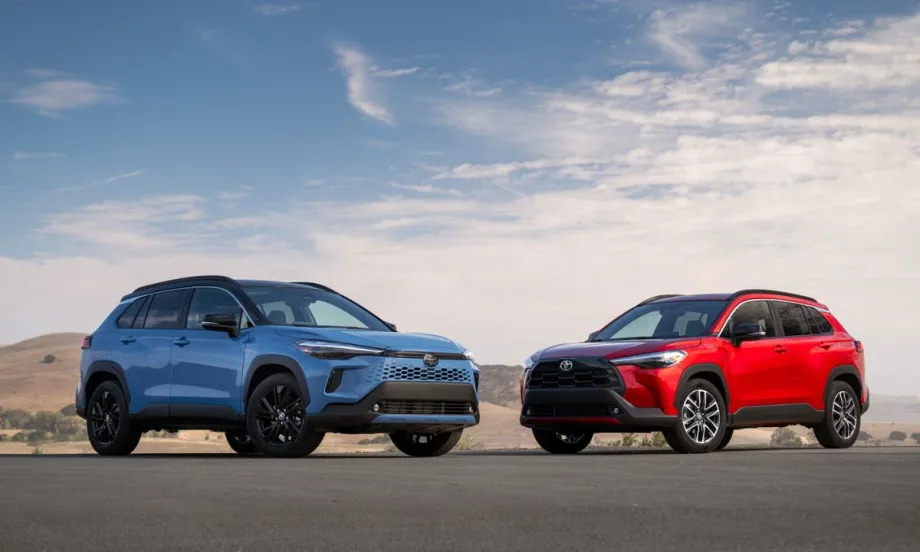 The 2026 Toyota Corolla Cross and its hybrid counterpart sit next to each other on the road with a blue sky background behind them.