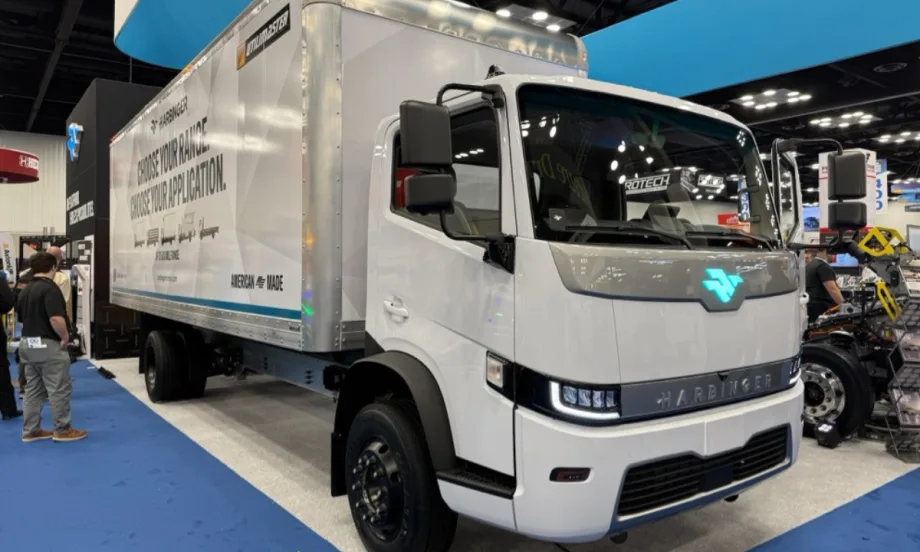 Harbinger HC Series Cab medium-duty electric work truck driving through a city with glass office towers, demonstrating the low cab forward fleet vehicle platform introduced at Work Truck Week.