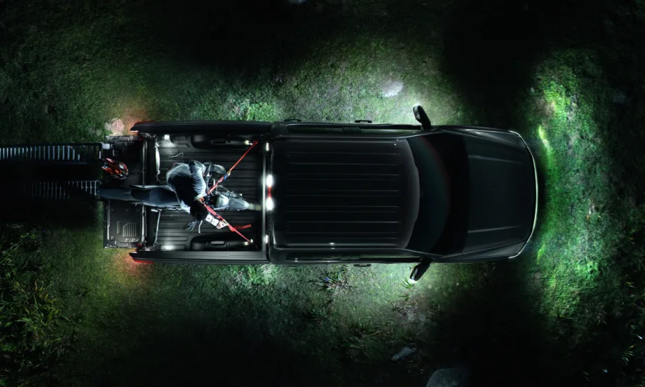 A nighttime aerial close-up of a Ford F-150 Lightning all-electric pickup truck with surround lighting parked on a grass field.