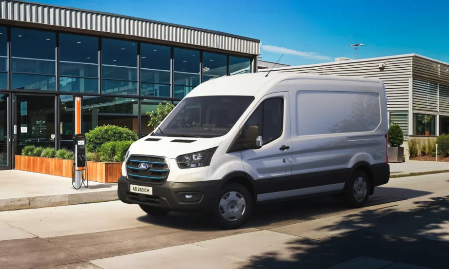 White Ford electric cargo van parked and charging at a ChargePoint station outside a modern commercial building.