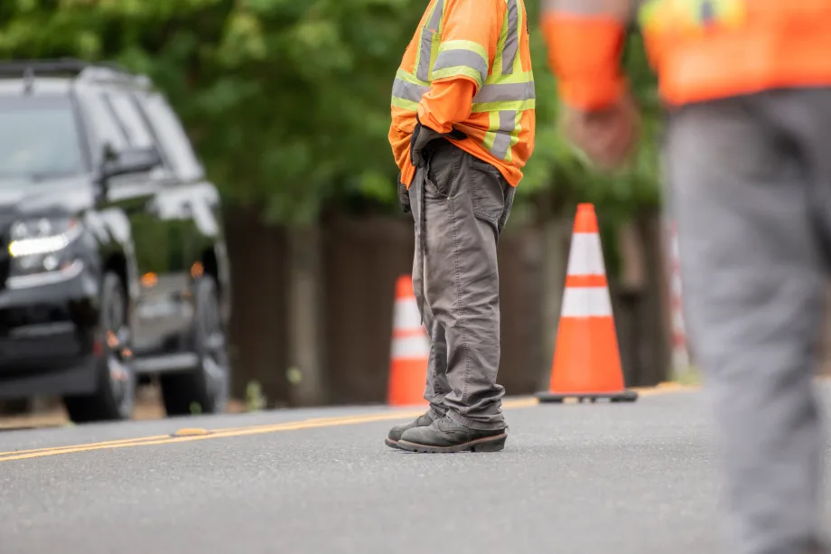 Man standing on the road with a road safety reflective vest on and safety cones on the road.