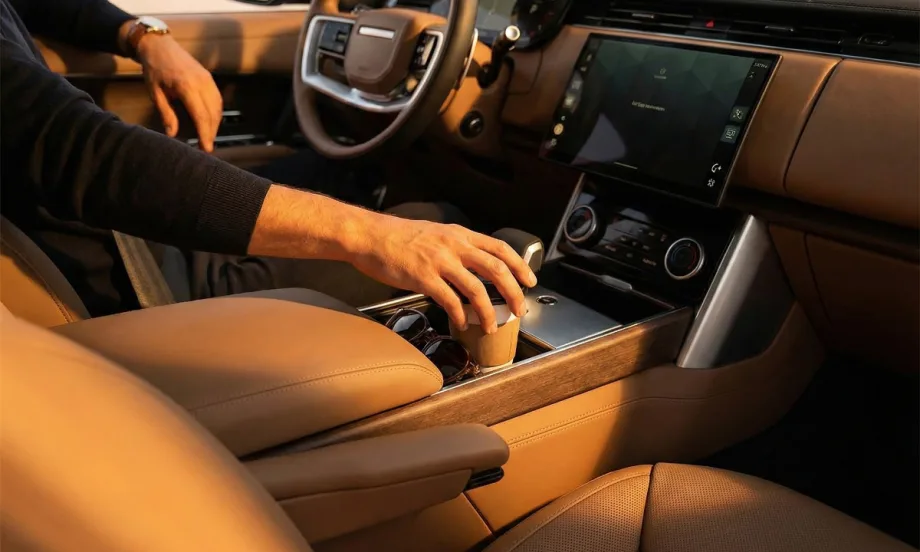 A driver seated in a luxury vehicle with leather surroundings and placing a coffee cup into the center console cup holder.