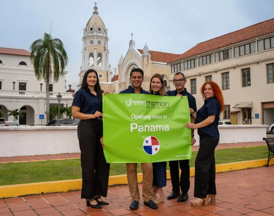 Five Panama-based Green Motion employees holding a green banner sign in front of historical building in Panama City, Panama.