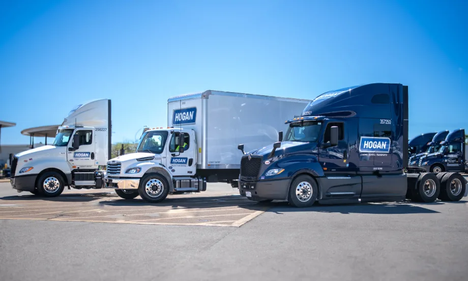 Three Hogan semi-trucks sit in a row in a parking lot on a sunny day.
