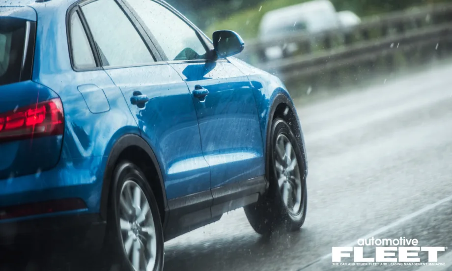 A blue SUV drives on wet pavement as rain comes down.