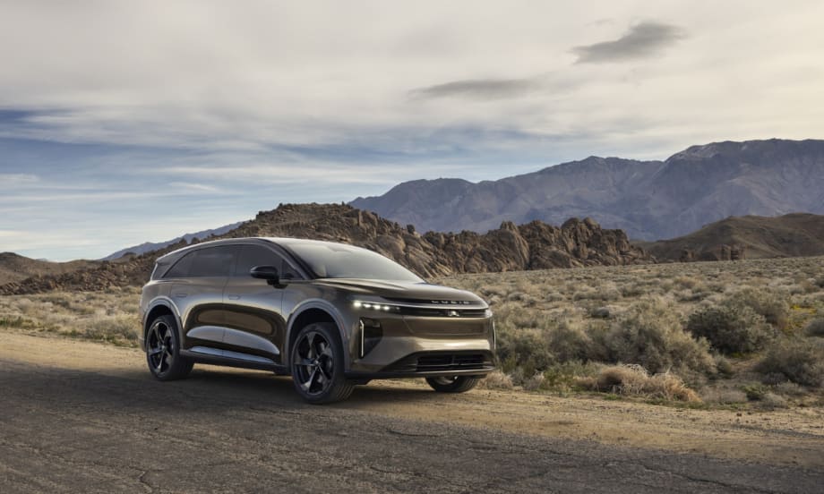 Lucid Gravity electric SUV parked on a desert road with mountains in the background, showcasing updated 2027 model with revised trims and added standard features.