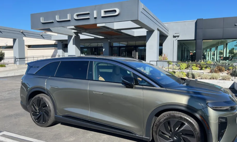 A right-side view of a gray Lucid Gravity Grand Touring in front of a Lucid dealership entrance.