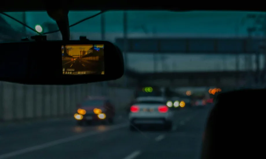 Looking through the windshield of a car from the interior, a dashcam is connected to the rearview mirror.