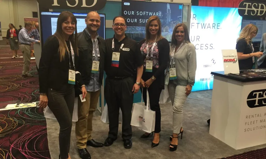 Five trade show attendees lined up in front of an exhibit booth.