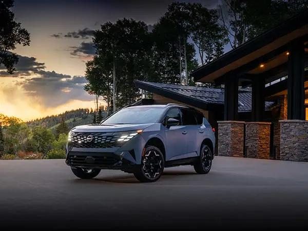 A grey Nissan drives on a road at sunset