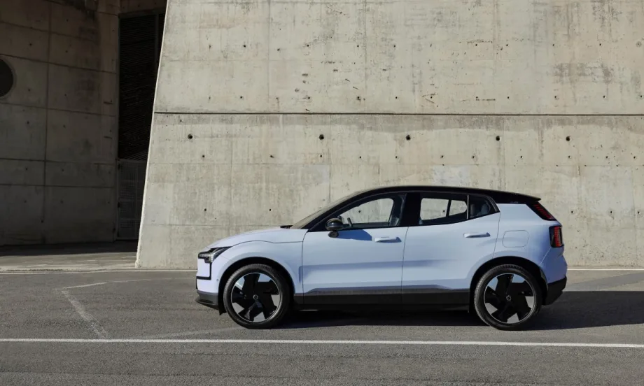 The left side view of a cloud blue 2025 Volvo EX30 parking in front of a gray concreate wall.
