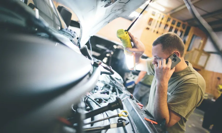 A man holding a light and a phone looking at the engine of a vehicle.