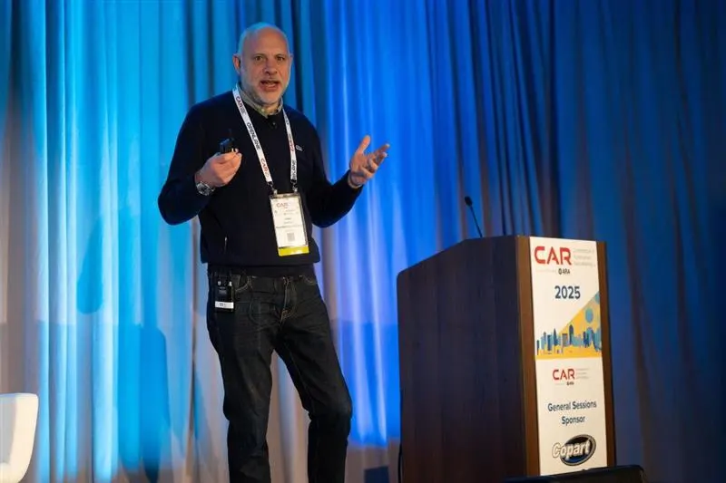 Speaker presenting on stage at the 2025 CAR Conference, standing beside a podium with event branding and sponsor logos.