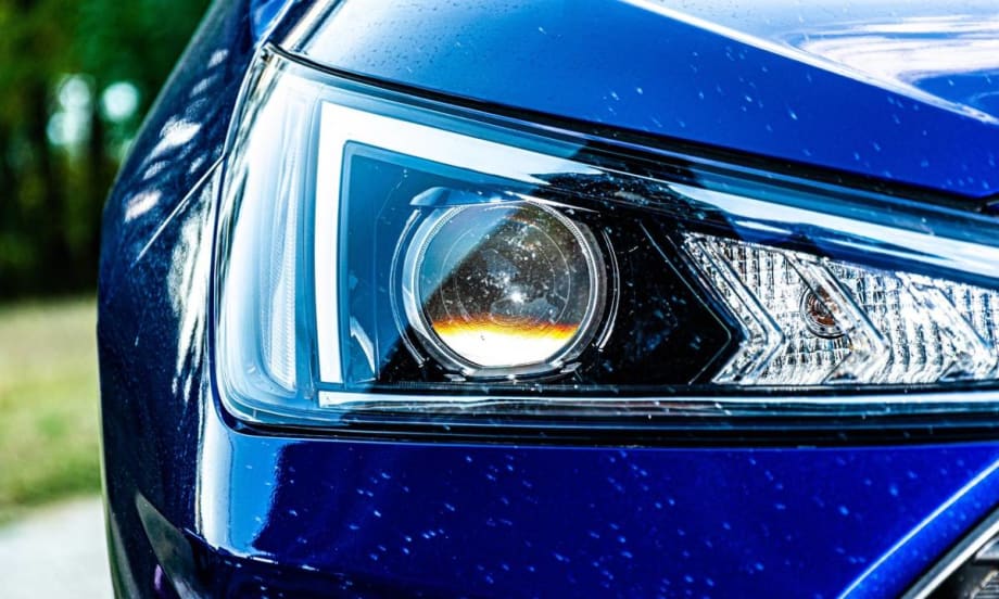 Close up of a blue car’s headlight with white marks or scratches on the surrounding auto body.
