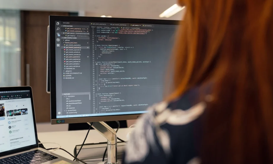 The back of worker positioned in front of two computer screens.