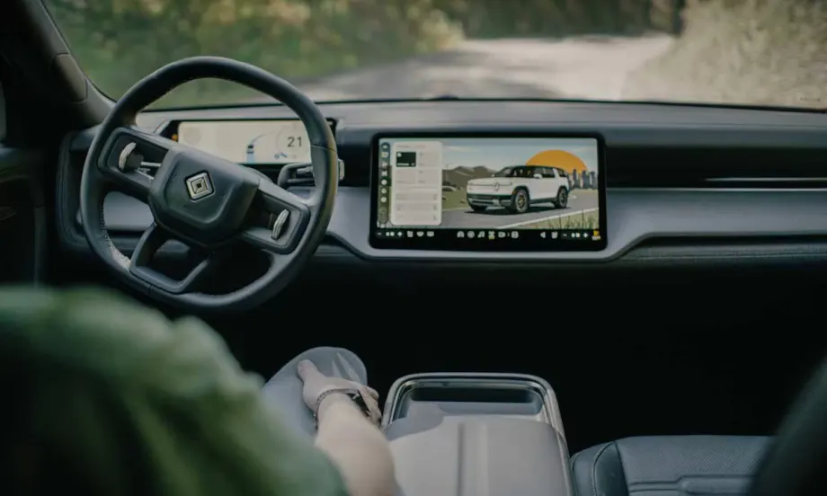 Interior view of a Rivian vehicle showing steering wheel and digital display screen with vehicle interface, representing autonomous technology development.