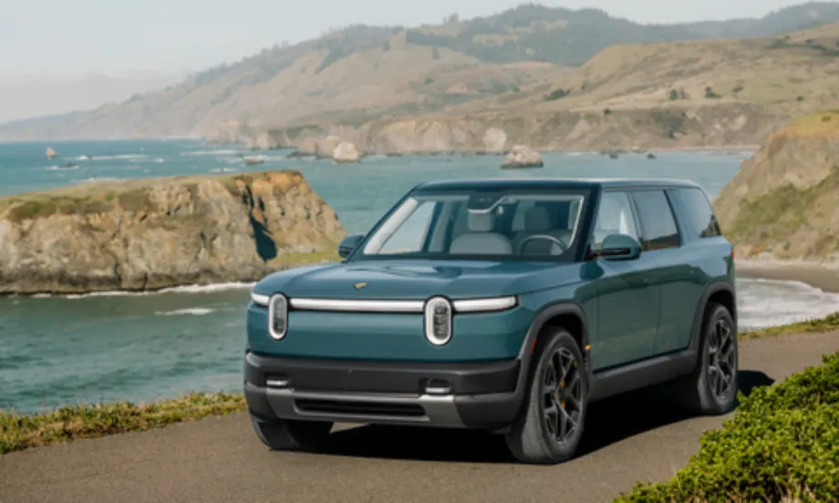 Rivian R2 electric SUV parked along a coastal road with ocean cliffs in the background, showcasing the midsize EV’s design and outdoor capability.