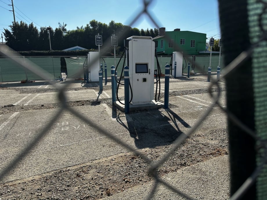 Empty EV chargers behind a chain link fence.
