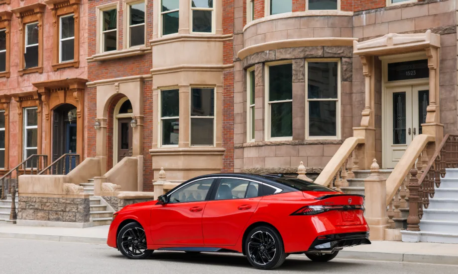 A 2026 red Nissan Sentra sits in front of a row of buildings.