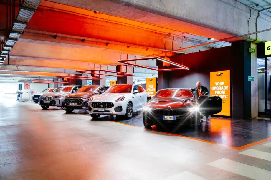 Rental car customer getting into a car parked in a line of SIXT rental cars at an airport in Milan, Italy.