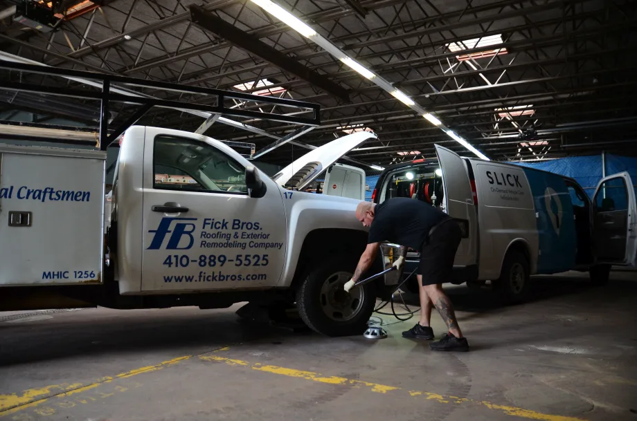 Technician services a commercial van inside a repair facility while a utility truck is parked beside it.