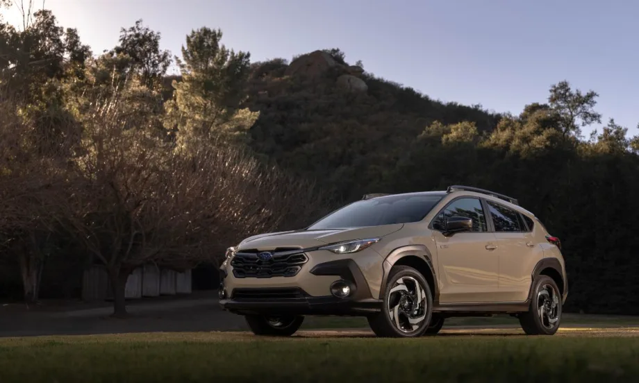 “A beige Subaru Crosstrek SUV parked on grass, surrounded by trees and hills under a clear sky at sunset.