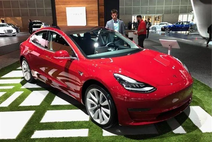 A bright shiny red Tesla 3 EV in a showroom.