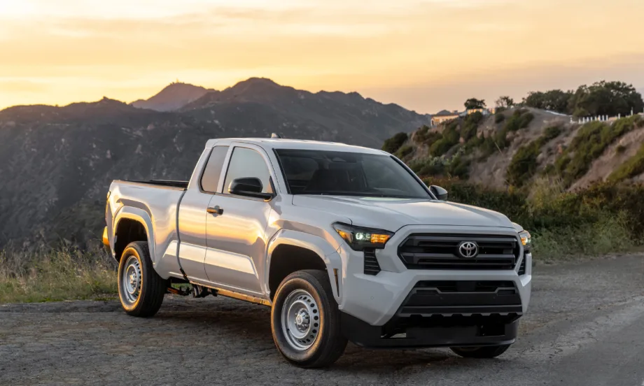A white 2026 Toyota Tacoma sits in a sunset landscape with mountains behind the road.