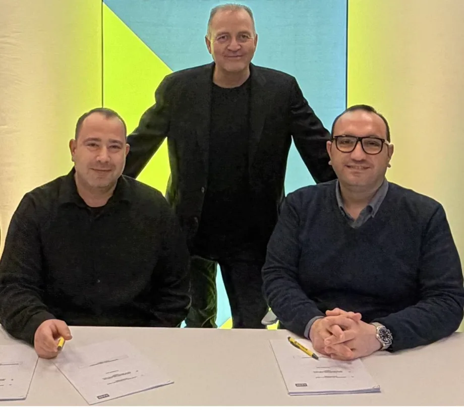 Three executives sitting and standing along a conference table with signed documents spread out.
