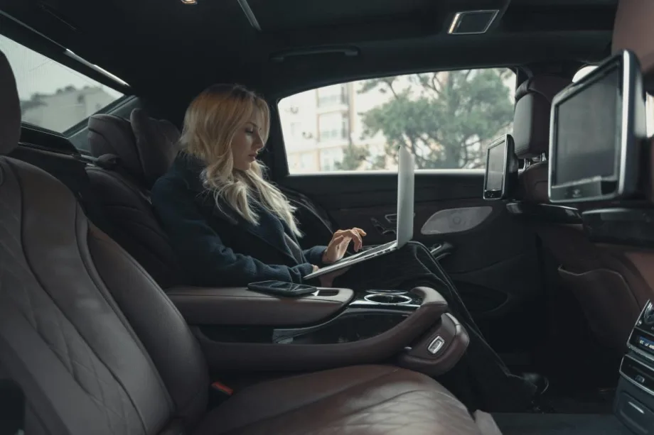 Businesswoman working on a laptop while riding in the backseat of a chauffeured car.