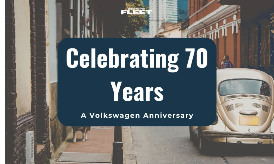 A vintage VW bug drives on a street between buildings.