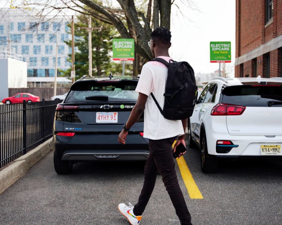 Man with a backpack walking behind carsharing vehicles.